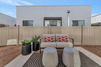 A modern outdoor living space with a white couch, two black planters, and a striped rug.